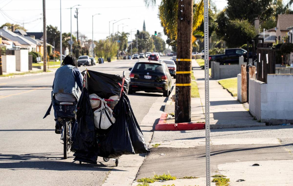 Johnny, un hombre sin hogar, recoge latas y botellas de plástico que almacena en el carro que tira con su bicicleta en una calle cerca del estadio SoFi, en Inglewood, California.
