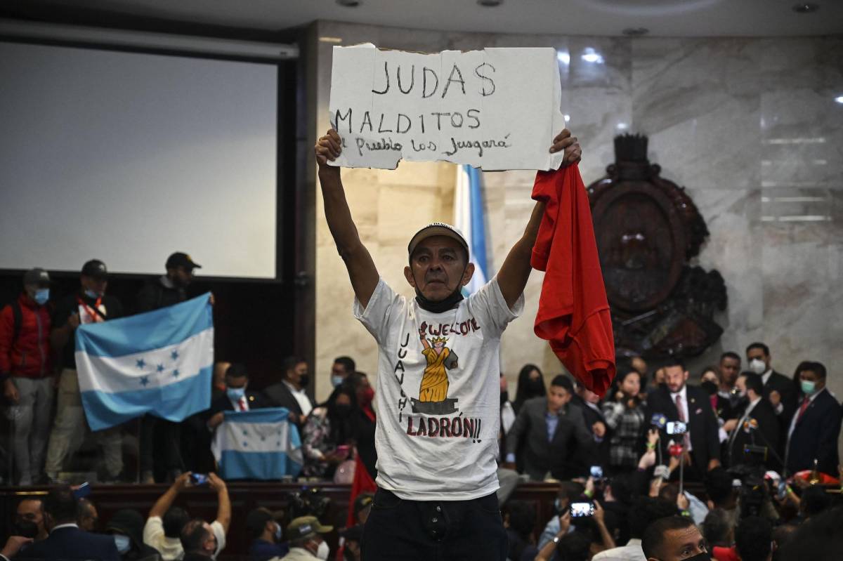 Un simpatizante del partido Libertad y Refundación (LIBRE) sostiene un cartel que dice “Maldito Judas, el pueblo te juzgará” al tomar posesión de la sede del Congreso de la República tras la elección de la Junta Directiva Provisional, en Tegucigalpa.
