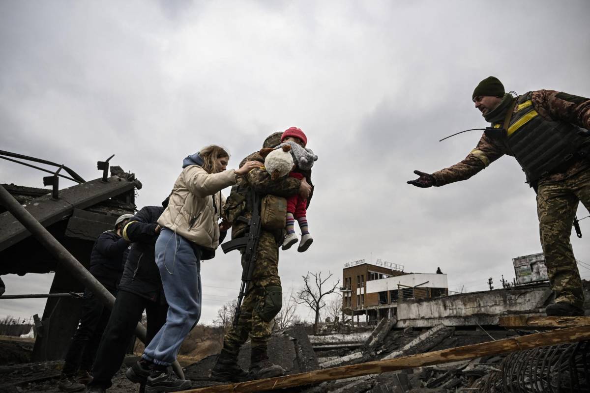 Un militar ucraniano lleva a un niño mientras ayuda a las personas a cruzar un puente destruido mientras evacuan la ciudad de Irpin, al noroeste de Kiev.