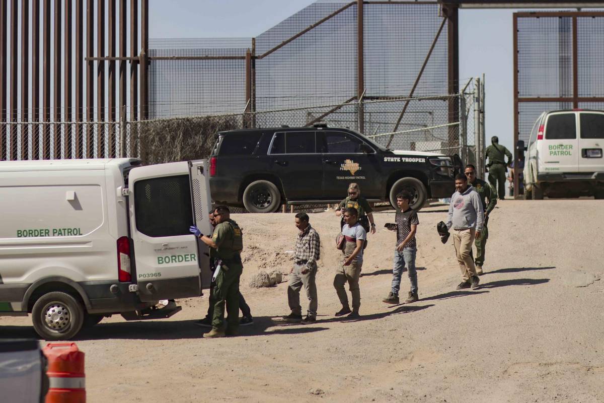 Migrantes detenidos son llevados hoy por miembros de la Patrulla Fronteriza estadounidense a un vehículo, junto al muro fronterizo en El Paso, Texas.