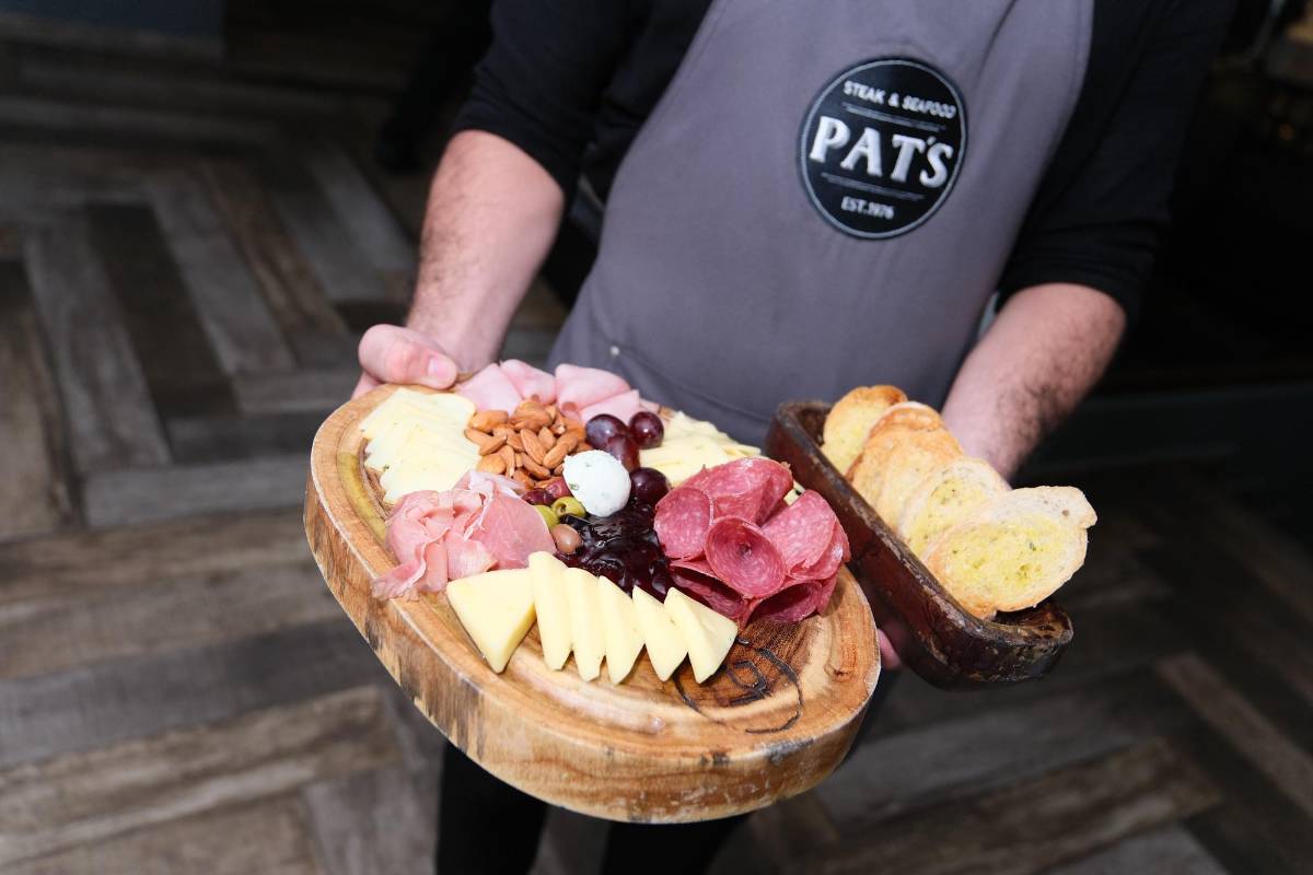 Un joven muestra la tabla con los deliciosos quesos y jamones.
