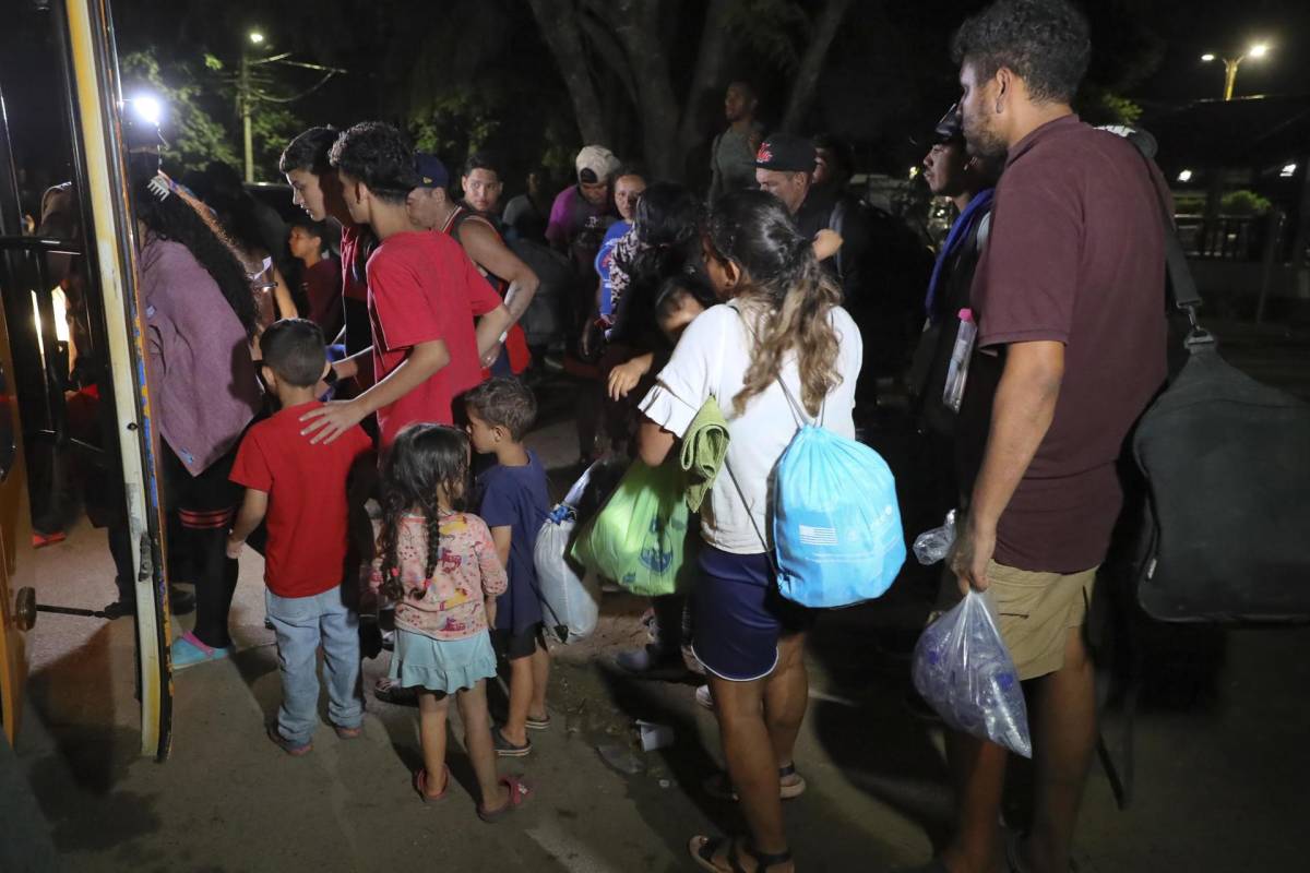 Familias de migrantes suben en la madrugada de hoy a un bus en la ciudad de Danlí, al oriente de Honduras.