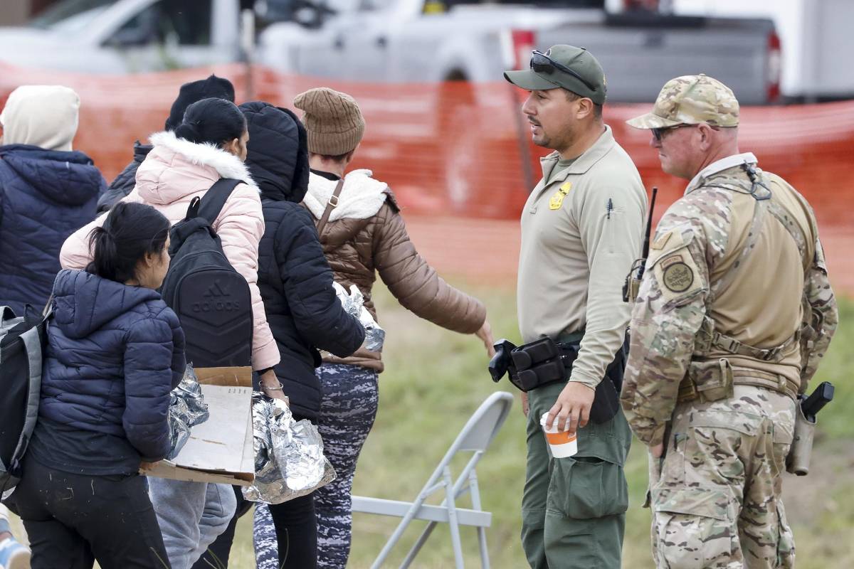 Fotografía de archivo donde se ve a un grupo de migrantes pasar frente a un agente de la Patrulla Fronteriza (C) y una Guardia Nacional de Texas (D) en Shelby Park en Eagle Pass, Texas, EE UU.
