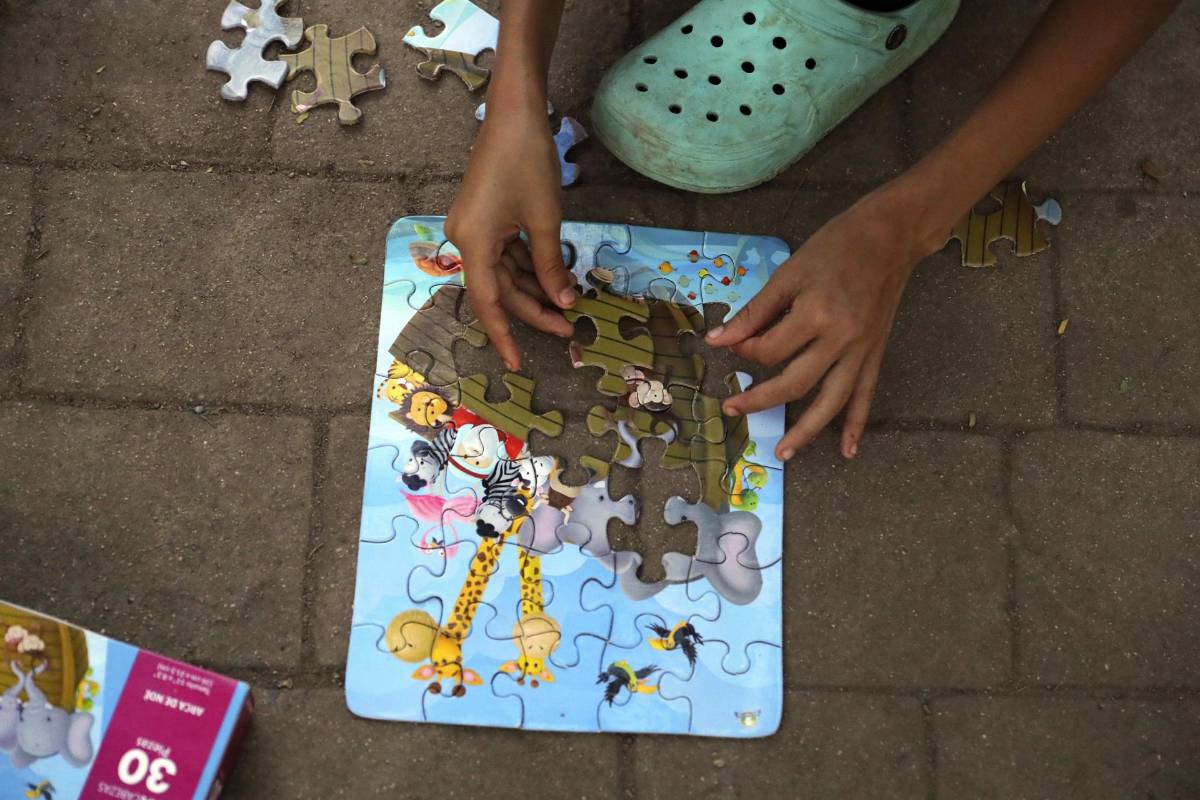 Una niña migrante juega hoy con un rompecabezas en el parque Monumento a la Madre en la ciudad de Danlí.