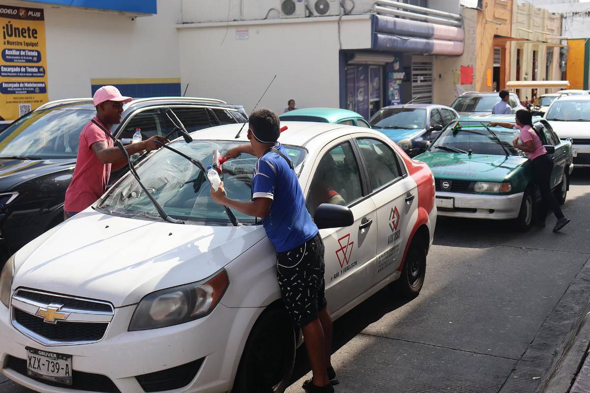 Migrantes limpian vidrios de autos en Tapachula a la espera de documentos para seguir avanzando hacia EEUU.