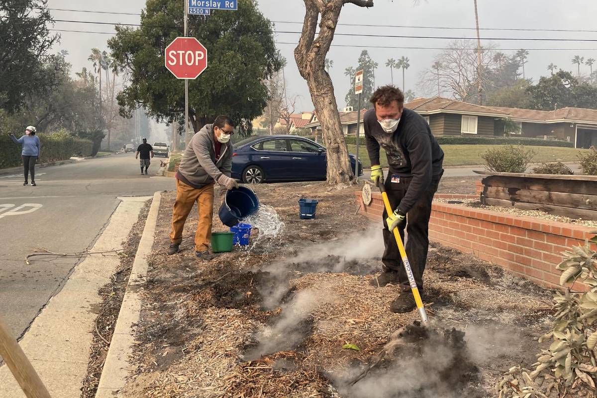 Unas personas vierten agua alrededor de las casas de un vecindario en Altadena, California (Estados Unidos).