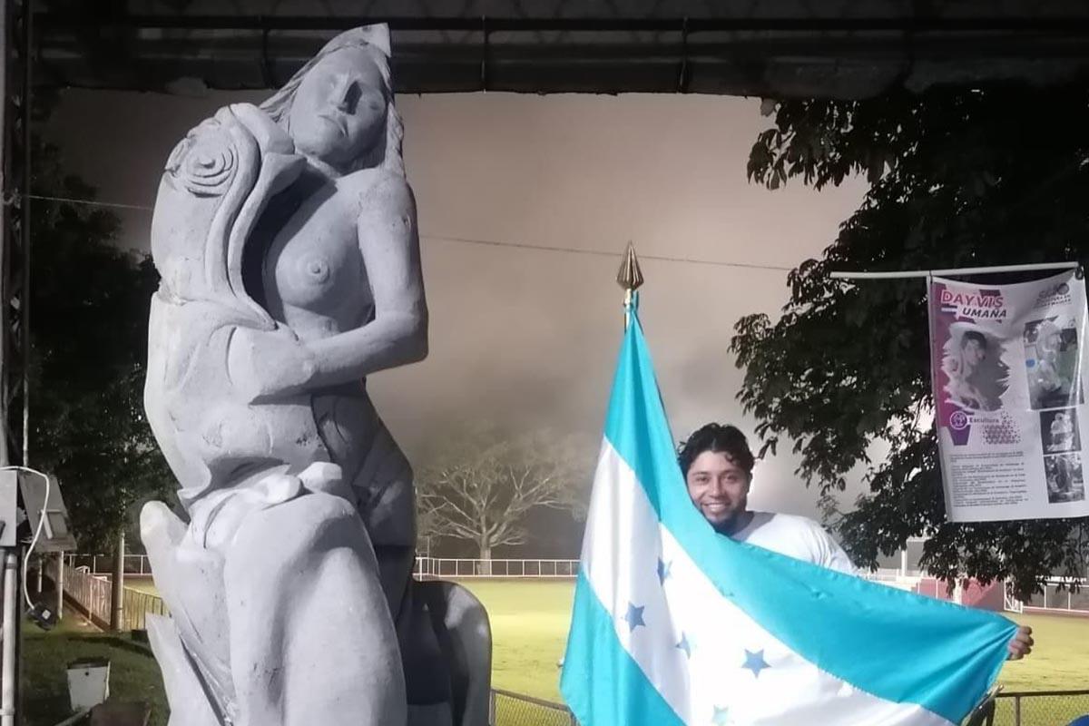El artista hondureño posa a la par de una escultura.