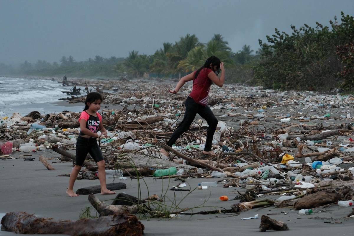 Niños juegan encima de desechos plásticos que llegan a las playas de Omoa.