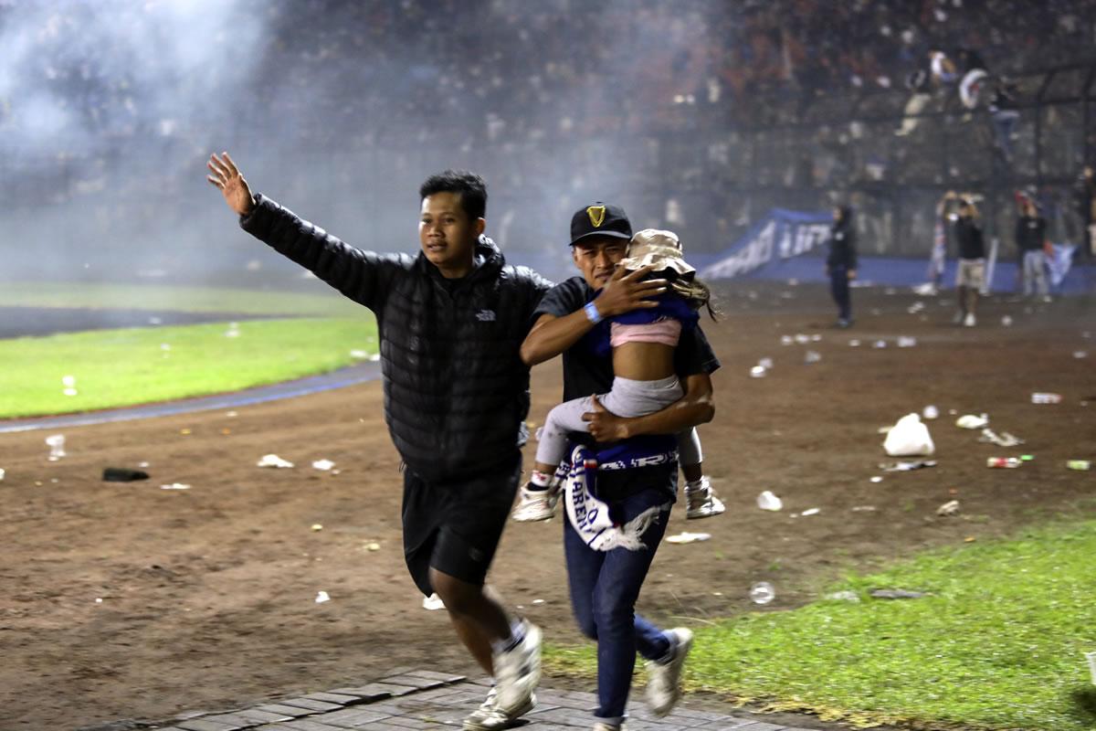 Dos hombres evacúan a una niña durante el enfrentamiento entre aficionados en el estadio Kanjuruhan.
