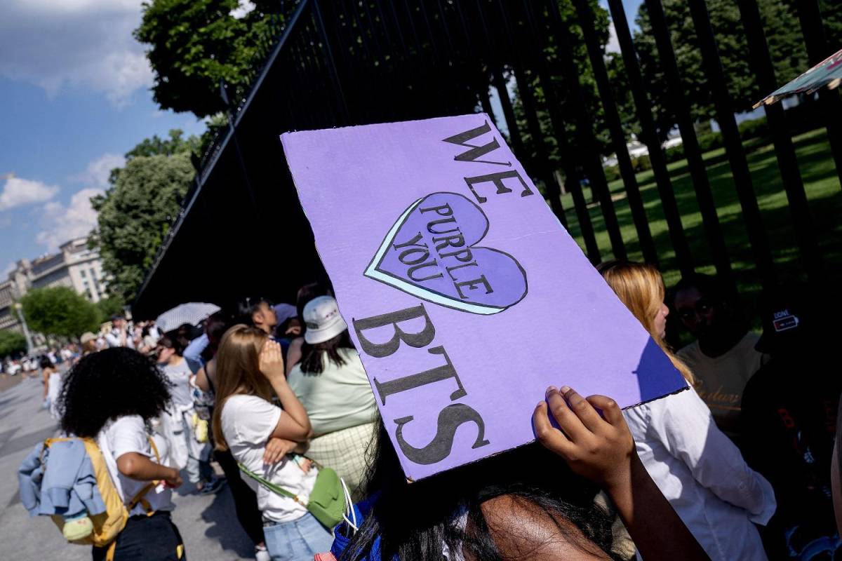 Un fanático de BTS usa un letrero para protegerse del sol, mientras espera con otros fanáticos afuera de la Casa Blanca en Washington, DC, el 31 de mayo de 2022.