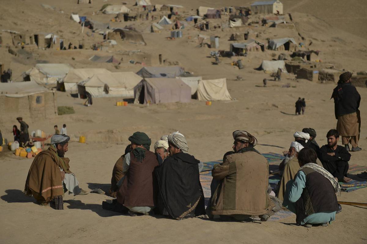 Un grupo de hombres se sienta en las afueras de un campamento de refugiados en Afganistán.