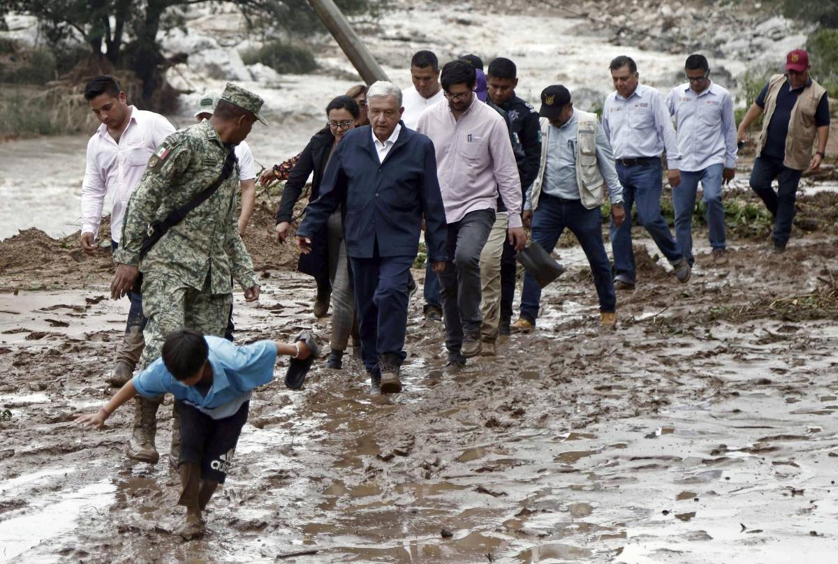 El presidente mexicano, Andrés Manuel López Obrador (C), y miembros de su gabinete caminan sobre el barro mientras visitan la comunidad del Kilómetro 42, cerca de Acapulco, estado de Guerrero, México, después del paso del huracán Otis, el 25 de octubre de 2023.