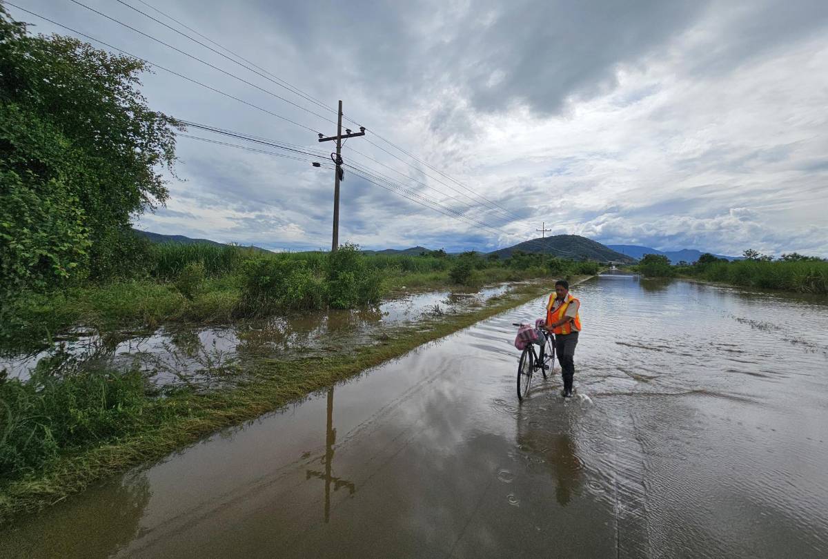 Una persona cruza con su bicicleta por una calle inundada en la comunidad de la Sabana, en San Manuel, Cortés (Honduras).