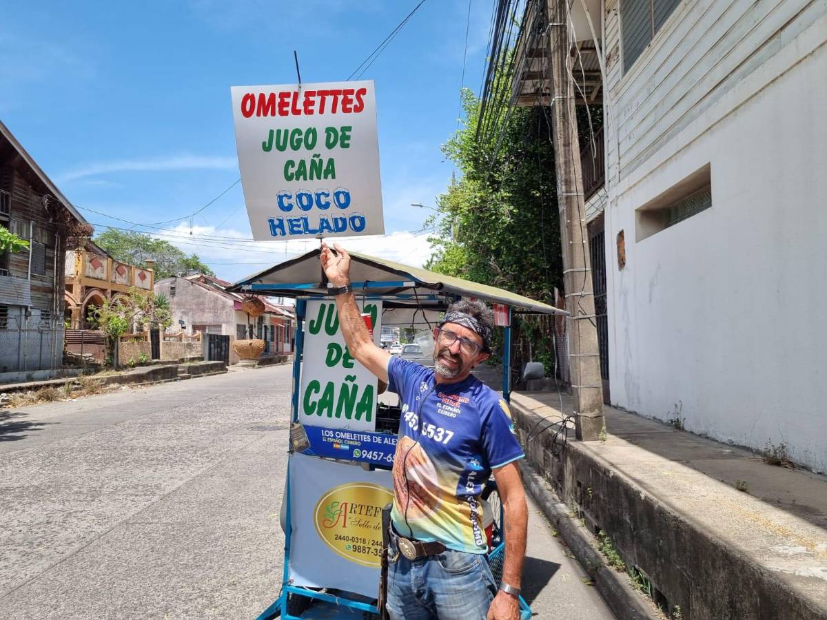 Álex posa junto a su troco que tiene un rótulo de “omelettes”, “jugo de caña” y “coco helado”.