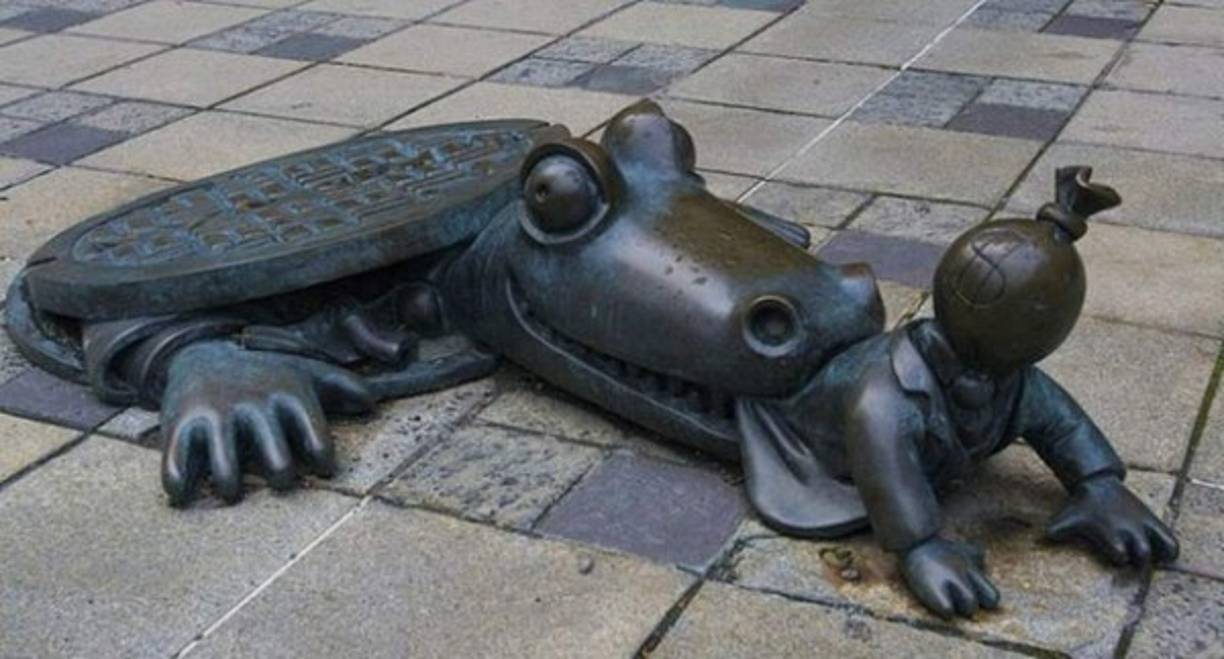 Un cocodrilo que devora un capitalista. Esta alegórica obra se encuentra en Brooklyn, Nueva York, USA.<br/>Imagen tomada de https://www.pinterest.com/mabemila/esculturas/