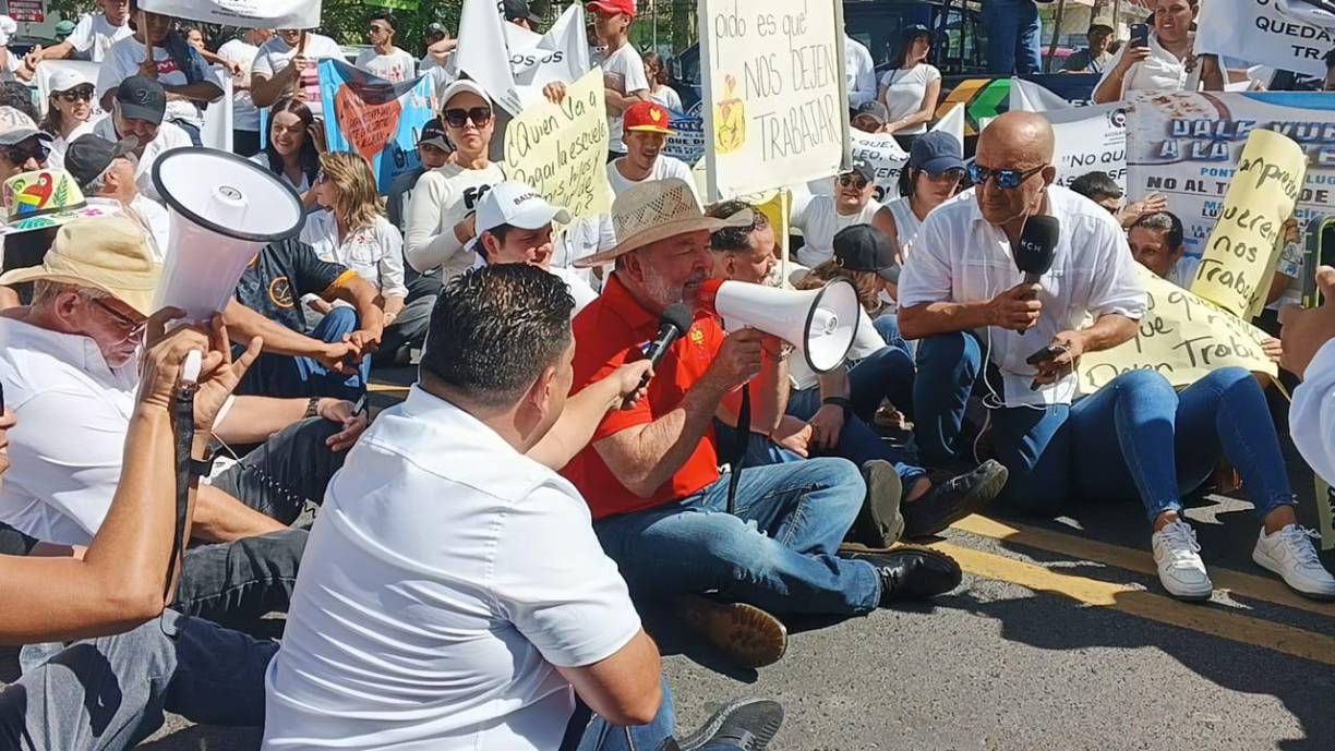 El alcalde Contreras habla a través de un megáfono en medio de una protesta que se desarrolla este lunes en San Pedro Sula en contra del toque de queda. 