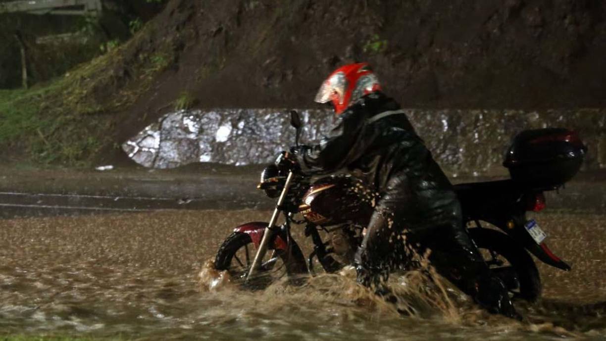Un hombre arrastra su motocicleta en una calle llena agua lluvia en Tegucigalpa.