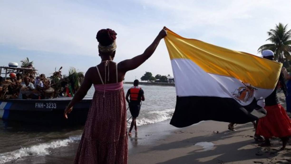 Una embarcacion trae a un grupo de músicos garinagu a la orilla de una playa en el norte de Honduras. La escena recuerda a su llegada por primera vez en 1797.