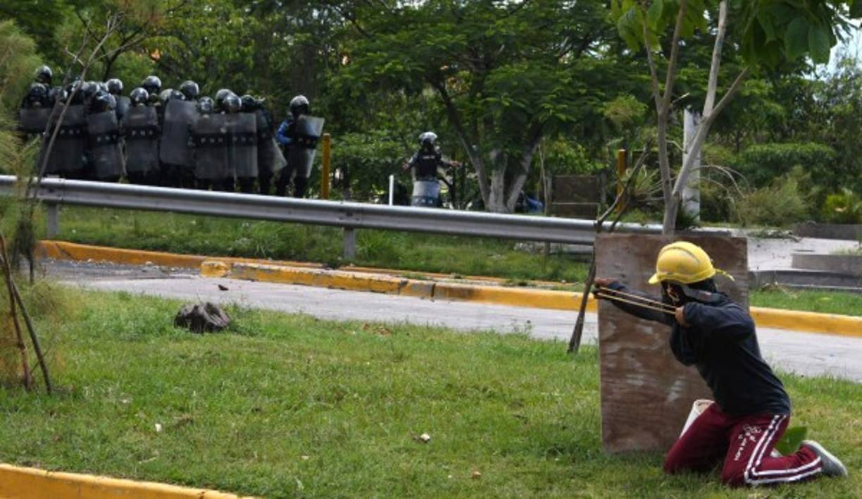 Los estudiantes encapuchados del Movimiento Estudiantil Universitario (MEU) se cubren de los gases lacrimógenos en el enfrentamientos con la policía en Tegucigalpa. AFP