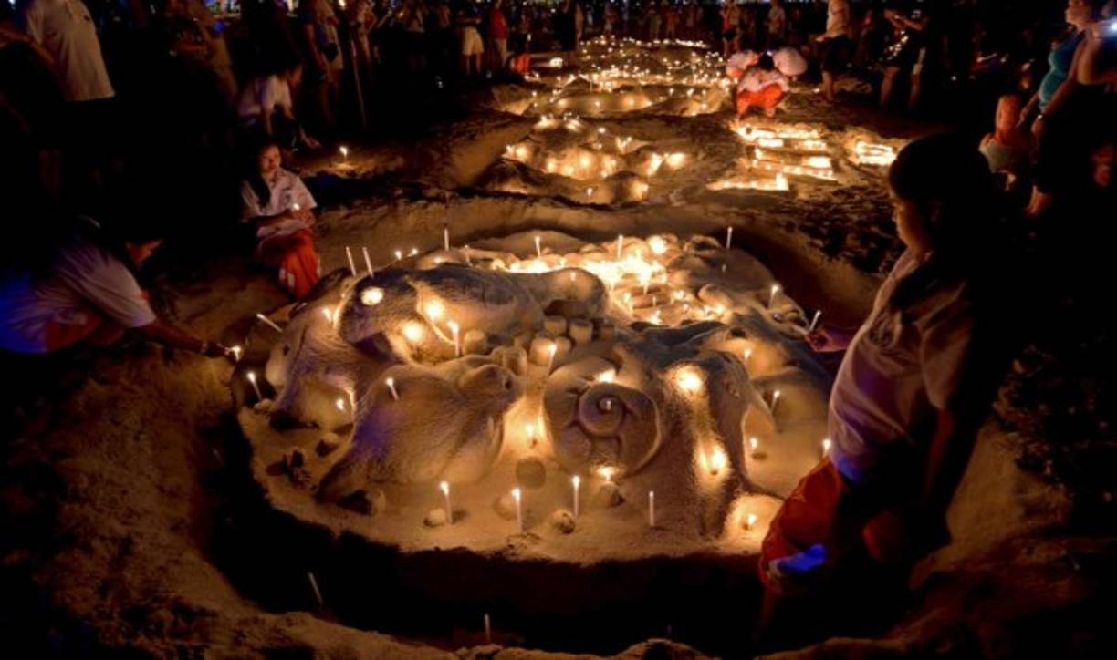 Estudiantes tailandeses colocan velas en una escultura de arena durante la conmemoración del décimo aniversario del tsunami de 2004 en la playa de Patong, en la provincia de Phuket.