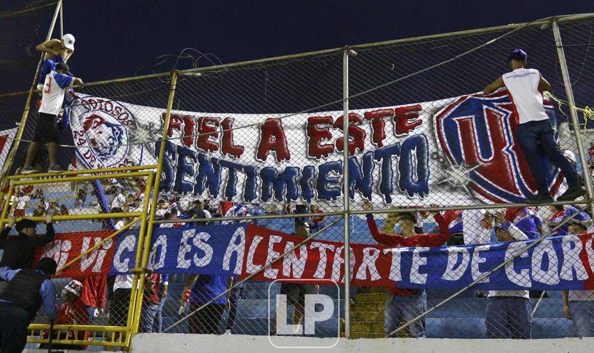 Miembros de la Ultra Fiel colocando una manta en el cerco de las gradas.