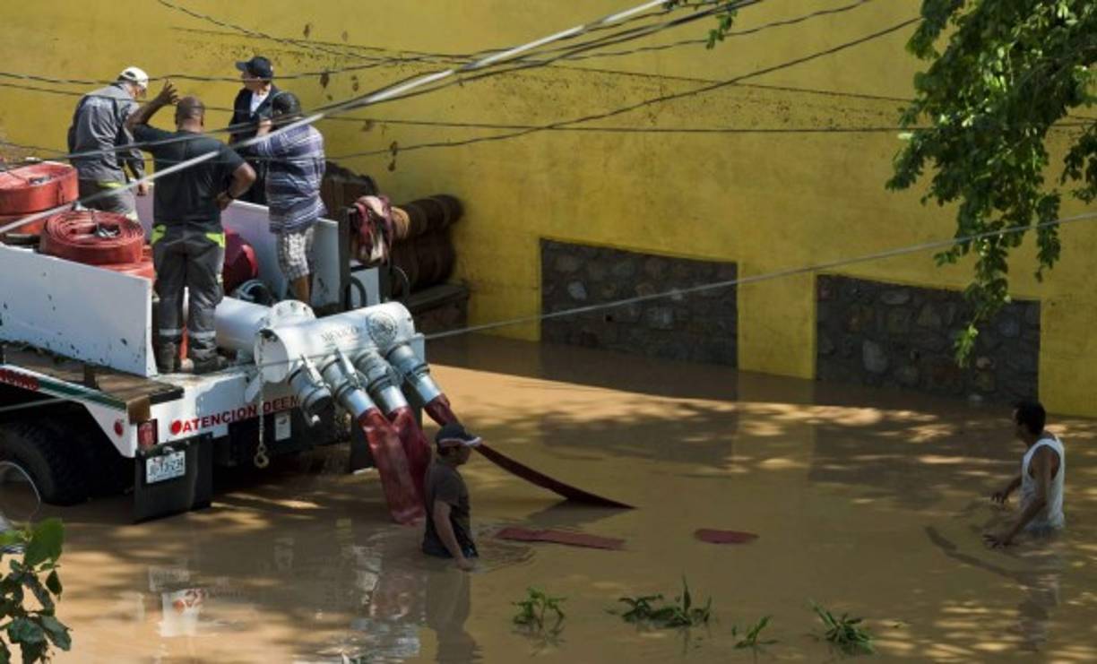 Bomberos colocan un bomba para extraer el agua que ha dejado en las calles el huracán Patricia.