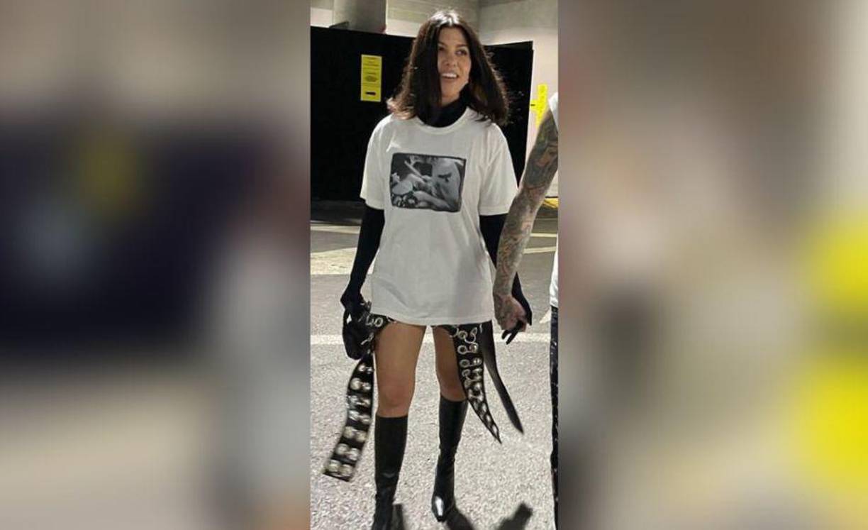 La estrella de Kardashians vestía una gran camiseta blanca sobre un cuello de tortuga negro que se conectaba perfectamente con un par de guantes de ópera negros. Llevaba botas negras hasta la rodilla y llevaba un pequeño bolso negro en una mano. De debajo de su camisa colgaban piezas de tela tachonadas con ojales de gran tamaño.