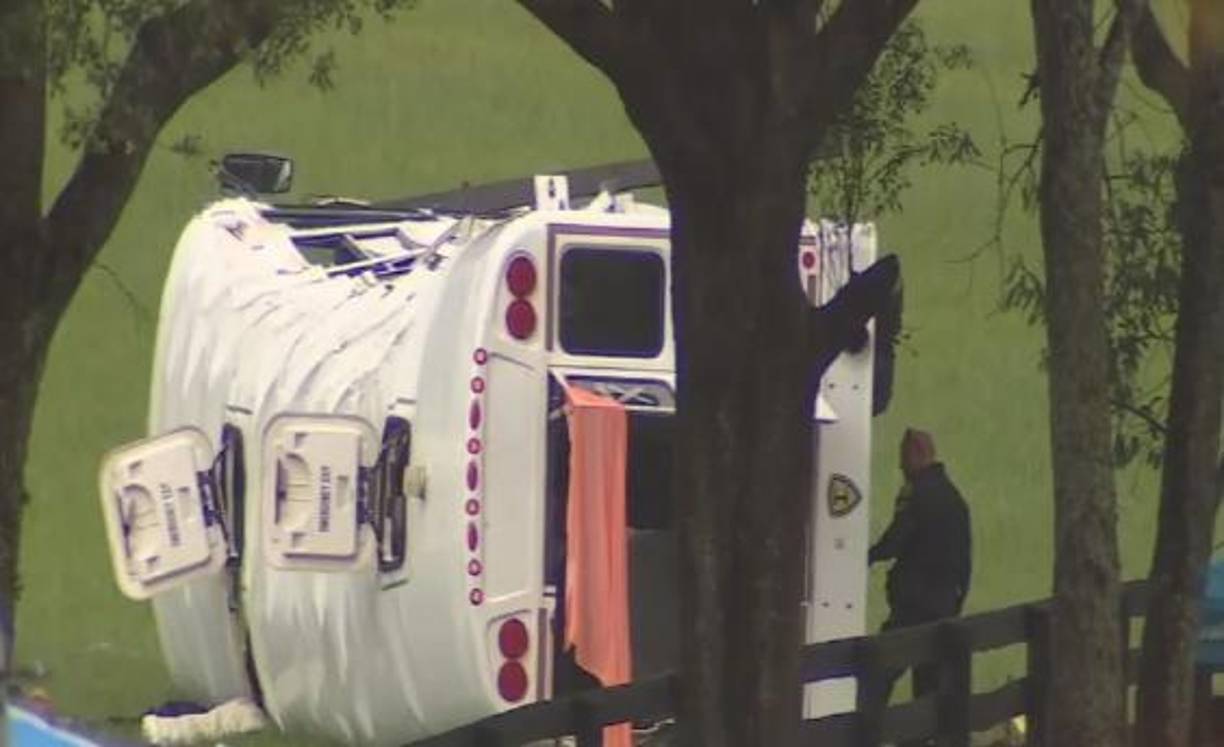 Imágenes del canal Fox muestran el autobús volcado al lado de una cerca de madera y árboles.