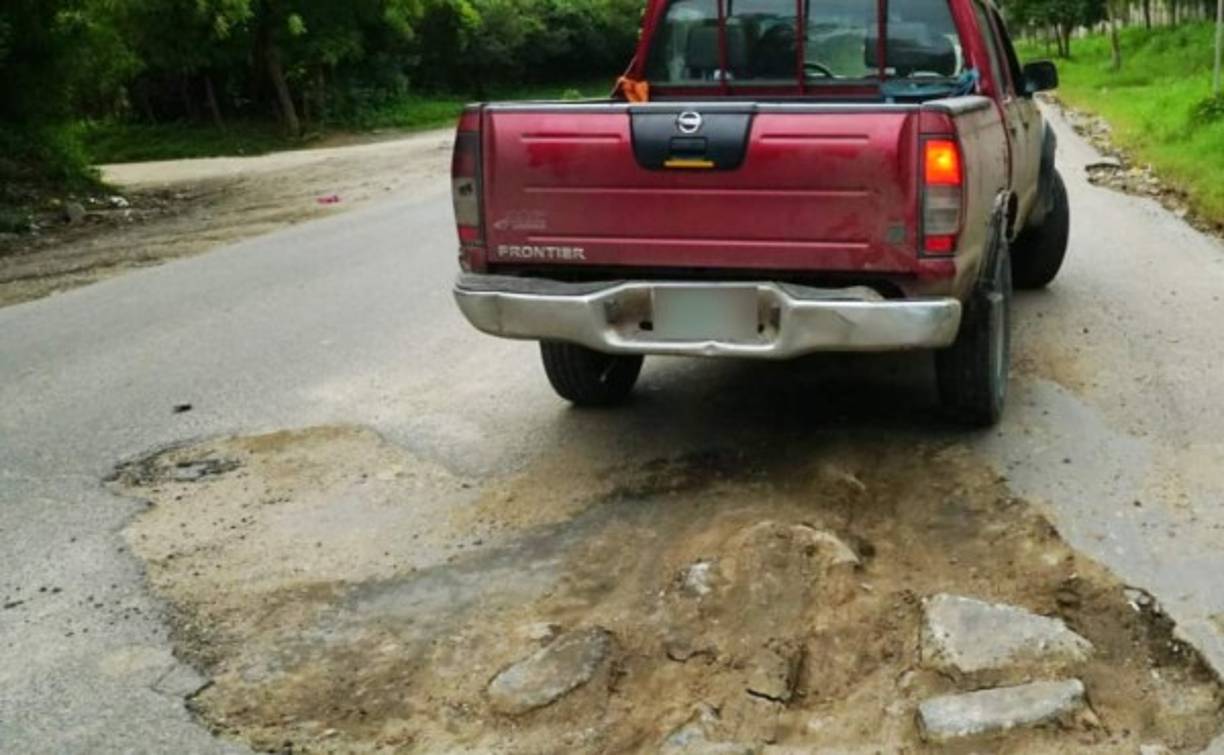 Pobladores de escasos recursos llegan la carretera y llenan de tierra y piedras los baches para amortiguar los daños en la misma.