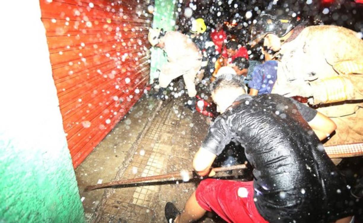 Los Bomberos y personas particulares trabajaron para abrir una de las cortinas del edificio en llamas.