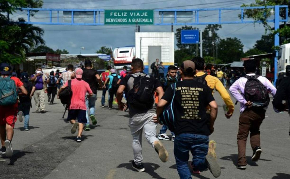 Los migrantes hondureños corren bajo un cartel que dice “Buen viaje, bienvenidos a Guatemala ”, luego de romper una cerca policial y entrar a Guatemala. Foto AFP