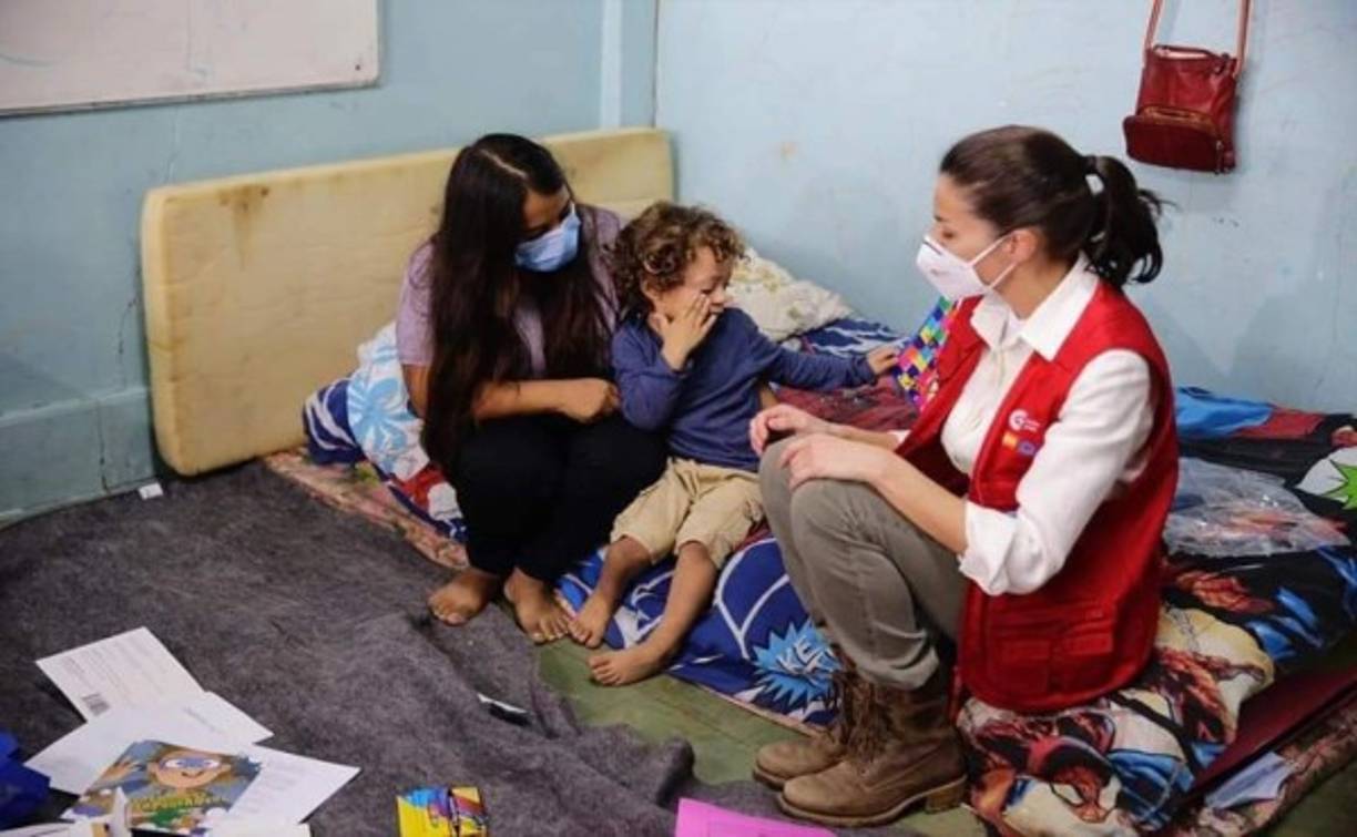 La Reina Letizia aparece sentada en una colchoneta mientras observa una madre y su hijo al interior del albergue en el Instituto Patria de La Lima.