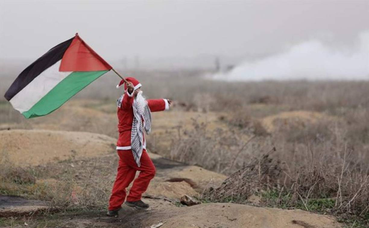 Un Santa Claus sostiene una bandera de Palestina.