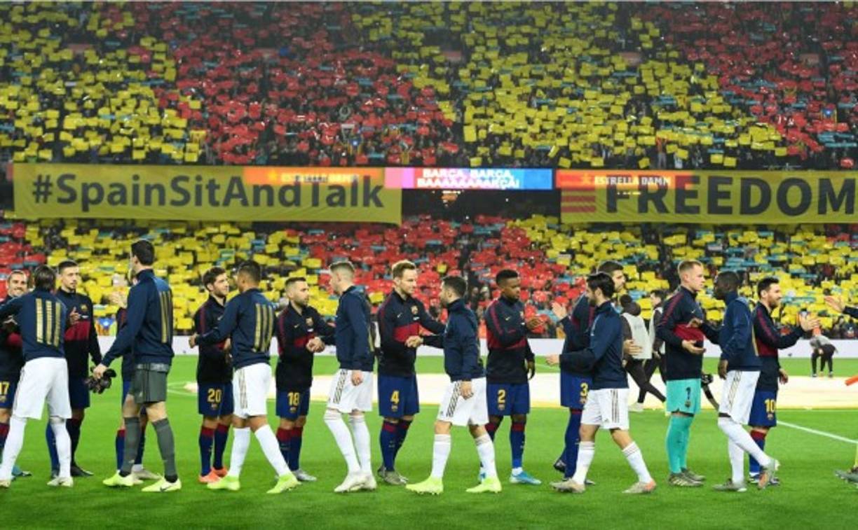Jugadores del Barcelona y Real Madrid se saludan antes del inicio del clásico. Al fondo, pancartas de los independentistas catalanes.