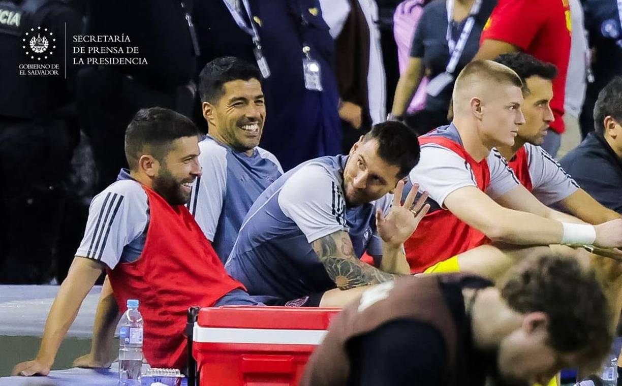 Lionel Messi saludando a los aficionados salvadoreños tras quedarse en el banquillo en el segundo tiempo. Luis Suárez y Jordi Alba sonríen.