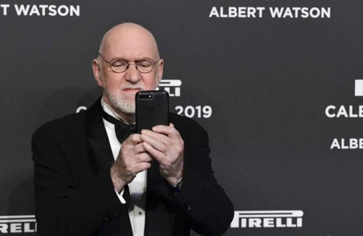 El fotógrafo escocés Albert Watson toma una foto con su teléfono inteligente mientras posa en la alfombra roja .