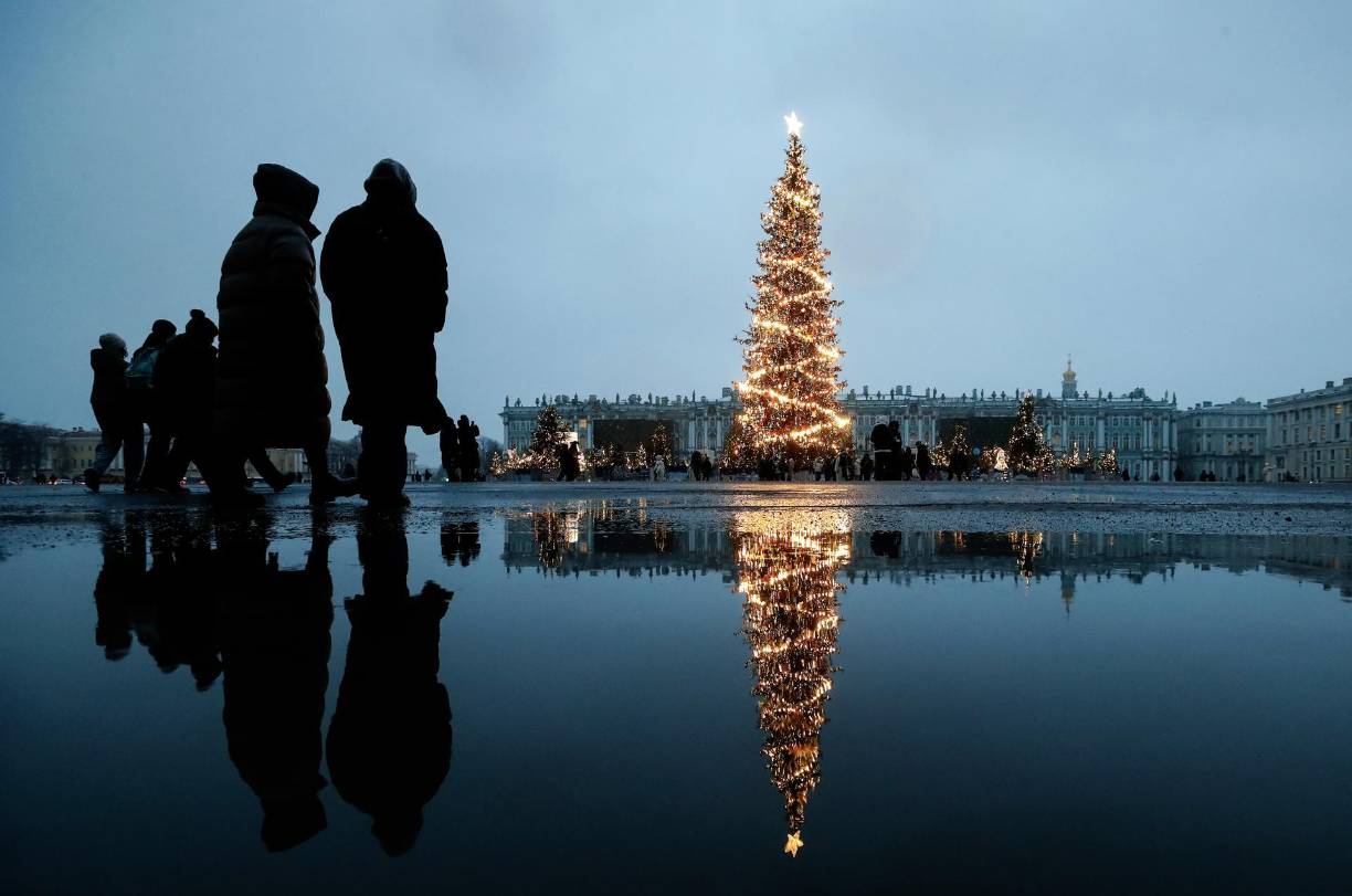 La gente se refleja en un charco mientras caminan por la Plaza Dvortsovaya (Palacio), decorada estacionalmente antes de las celebraciones de Año Nuevo y Navidad, en San Petersburgo.