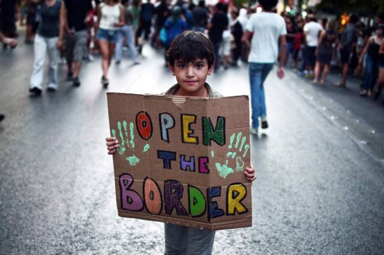 Un niño sostiene un cártel en el que se lee, 'abran las fronteras', durante una manifestación en pro de los refugiados en Grecia.