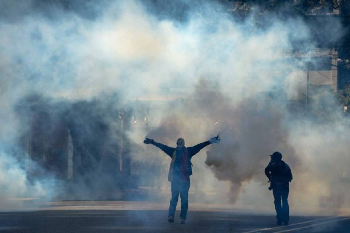 Un manifestante con máscara antigás camina en medio del humo y los gases lacrimógenos.