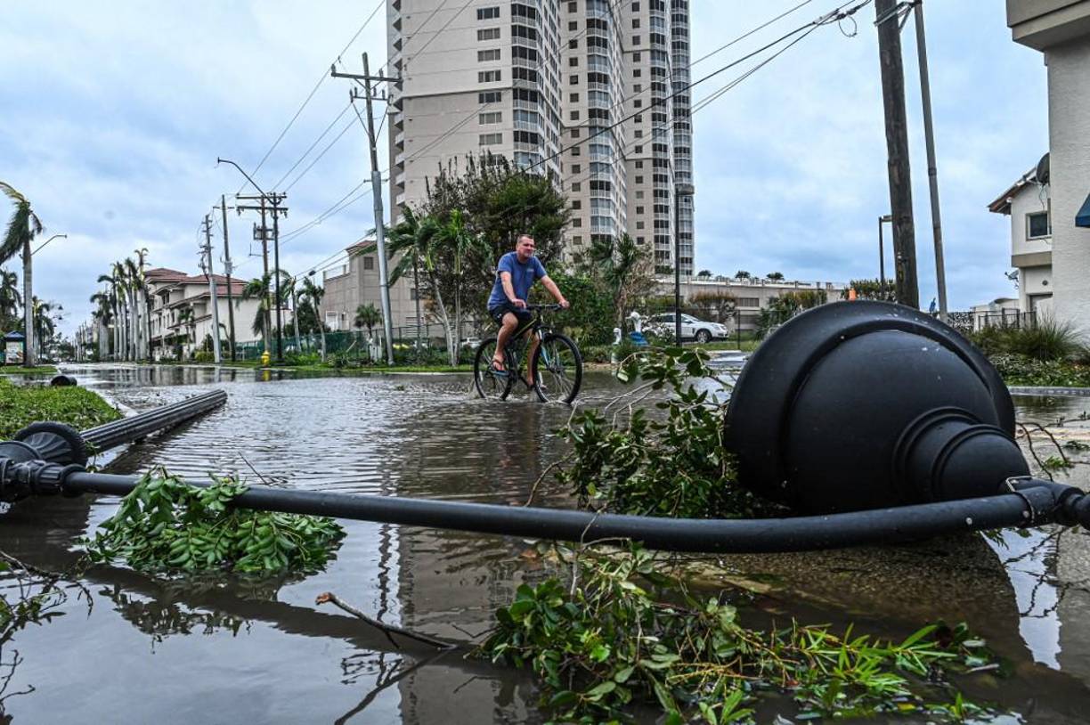 Un hombre monta en bicicleta a través del agua pasando una farola caída después del huracán Ian.