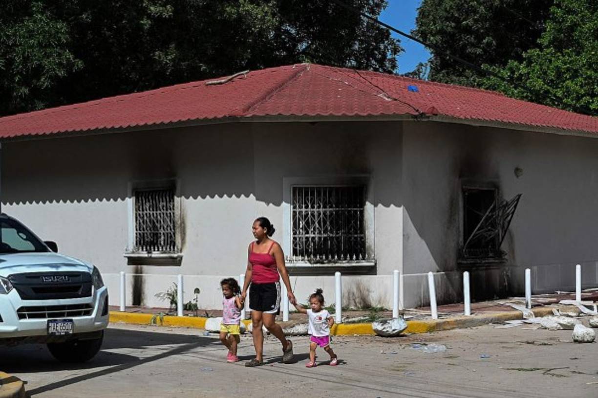 Una mujer con sus hijos pasa junto a la casa quemada del ciudadano italiano Giorgio Scanu en el municipio de Santa Ana de Yusguare en Choluteca. AFP