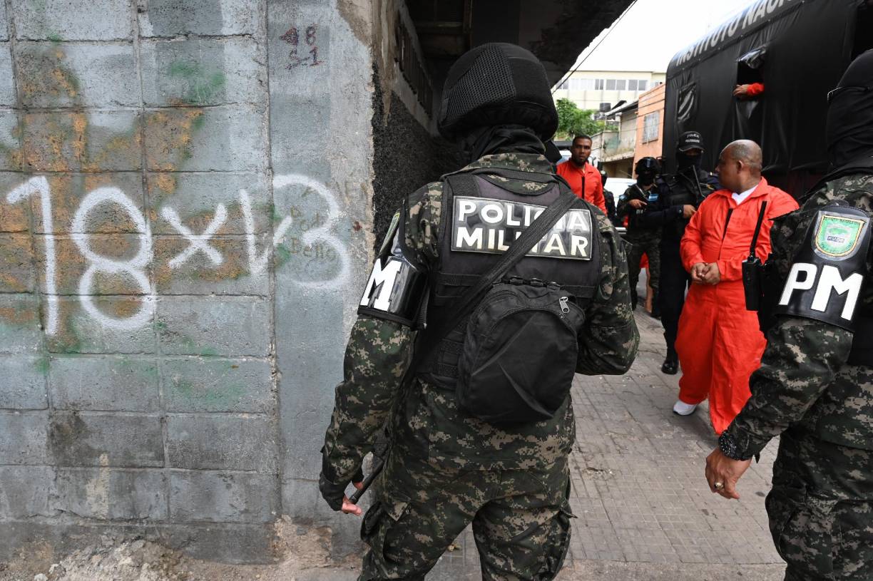 Members of the Military Police of Public Order (PMOP) guard inmates as they erase graffiti alluding to the Barrio 18 and Mara Salvatrucha (MS-13) gangs in Tegucigalpa on July 8, 2024. Inmates held in the Tamara National Penitentiary Center, 20 km north of the capital, went out handcuffed to erase graffiti as part of their social reinsertion. (Photo by Orlando SIERRA / AFP)
