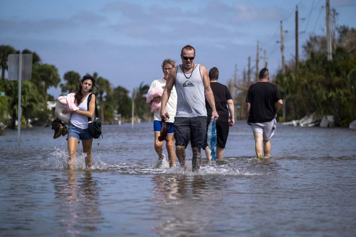 Las personas llevan sus pertenencias mientras caminan por el agua en un vecindario inundado después del huracán Ian en Fort Myers. 