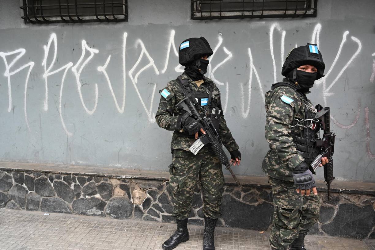 Members of the Military Police of Public Order (PMOP) guard while inmates (out of frame) erase graffiti alluding to the Barrio 18 and Mara Salvatrucha (MS-13) gangs in Tegucigalpa on July 8, 2024. Inmates held in the Tamara National Penitentiary Center, 20 km north of the capital, went out handcuffed to erase graffiti as part of their social reinsertion. (Photo by Orlando SIERRA / AFP)