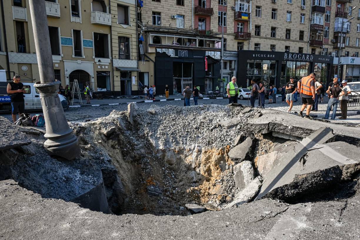 Municipal service workers stand around a crater following an overnight missile strike in Kharkiv on August 27, 2022, amid the Russian invasion of Ukraine. (Photo by SERGEY BOBOK / AFP)