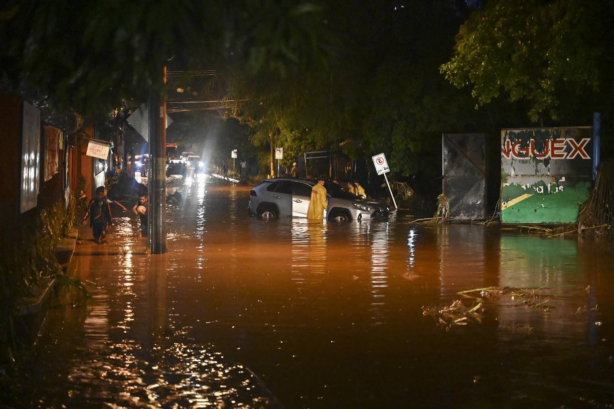 Members of the Fire Brigade assist the driver of a car which was stranded due to heavy rains in Tegucigalpa, on May 20, 2022. - Some 100 houses and at least 600 people were affected when the La Orejona and La Salada streams, which cross the capital, overflowed their banks, according to the Fire Brigade. The heavy rains are the result of a tropical wave passing through Honduran territory. (Photo by Orlando SIERRA / AFP)