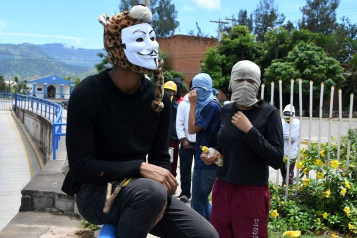Los estudiantes encapuchados del Movimiento Estudiantil Universitario (MEU) se cubren de los gases lacrimógenos en el enfrentamientos con la policía en Tegucigalpa. AFP