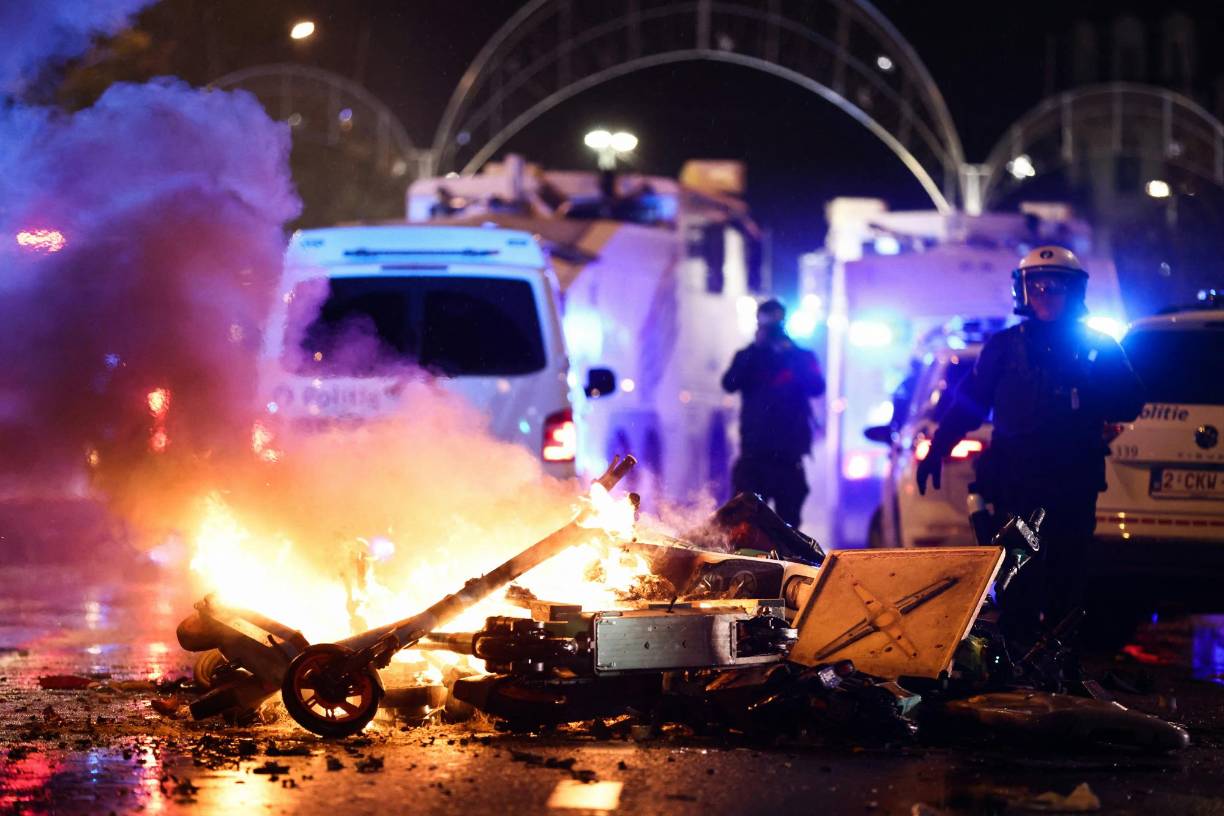 A police officer walks past burning eletrical scooters on the sideline of the live broadcast of the Qatar 2022 World Cup Group F football match between Belgium and Morocco, in Brussels, on November 27, 2022. - Violence broke out in Brussels on November 27, 2022 after Morocco's victory over Belgium at the World Cup, with "dozens of people" attacking street furniture and police, police said. (Photo by Kenzo TRIBOUILLARD / AFP)