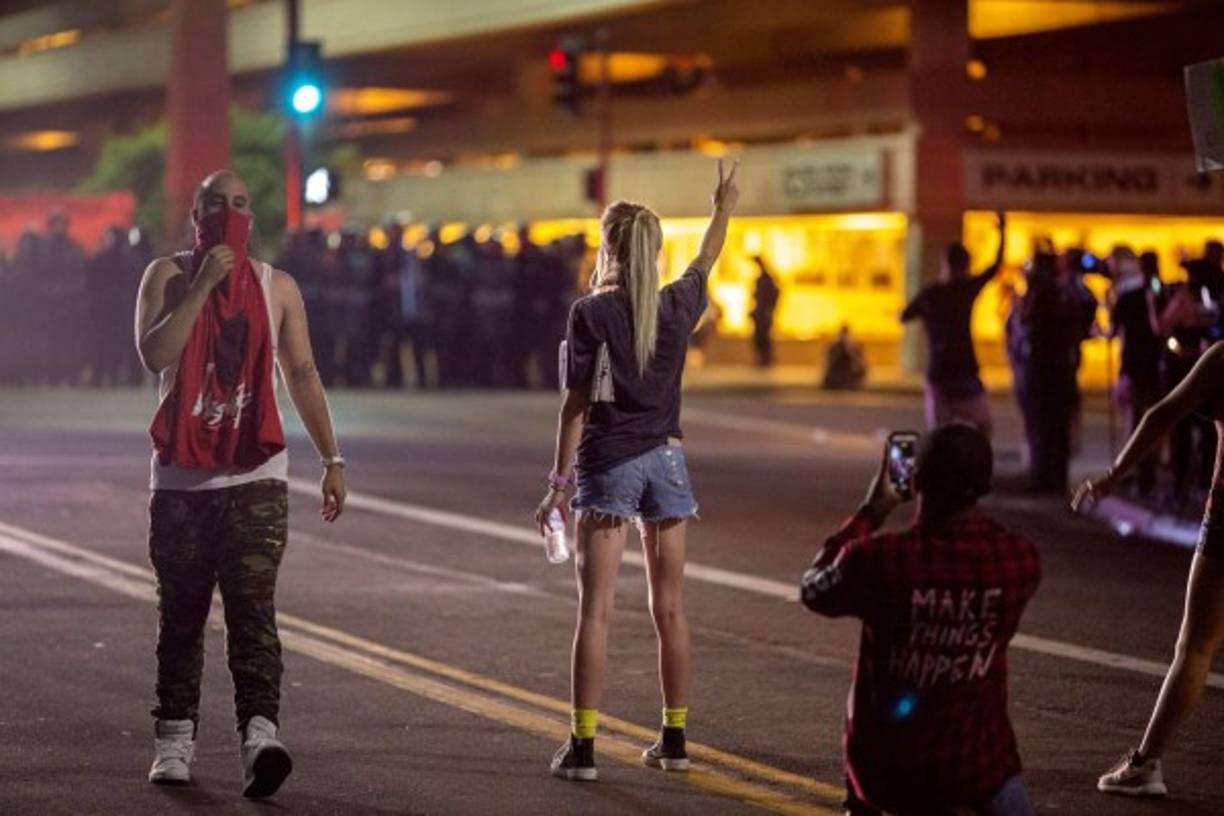 Una manifestante hace un símbolo de paz frente a los agentes antimotines durante una protesta contra Trump en Arizona.