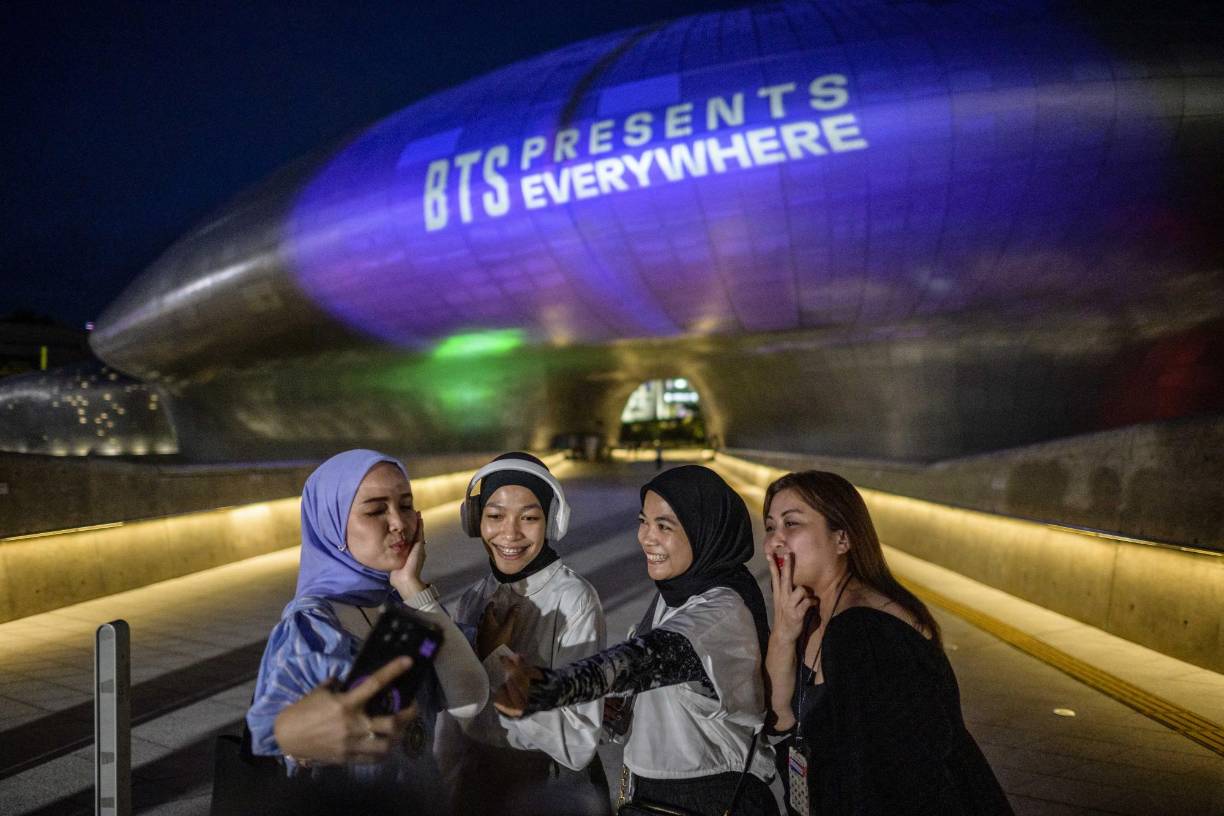 Los fanáticos se toman una selfie frente a Dongdaemun Design Plaza mientras se ilumina con luz púrpura.